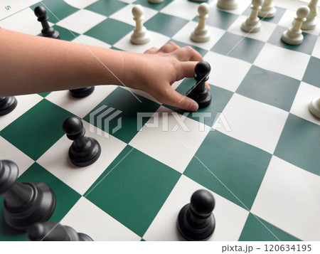 Childs hand holding chess pawn on green and white chessboard 120634195