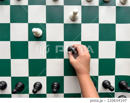 Hand holding chess piece on vertical chessboard with green and white squares Hand holding chess piece on vertical chessboard with green and white squares 120634197