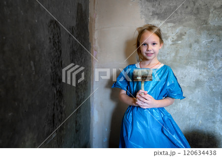 9-year-old girl in blue workwear priming a cement wall. Renovation concept. 120634438