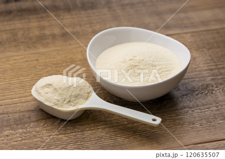 木目のテーブルに計量スプーンと器に入ったプロテイン 120635507