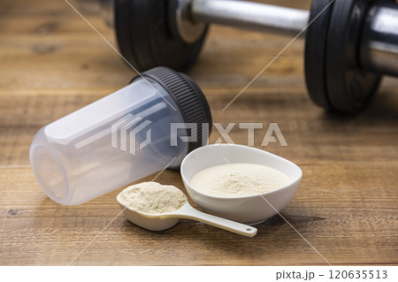 筋トレ準備に置かれたプロテインと計量スプーンとシェイカーとダンベル 120635513