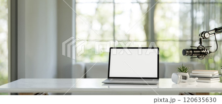 A laptop, headphones, and a microphone on a white table in a modern bright living room. 120635630