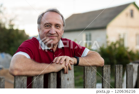 Mature man standing relaxed near fence in backyard smiling Mature man standing relaxed near fence in backyard smiling 120636216