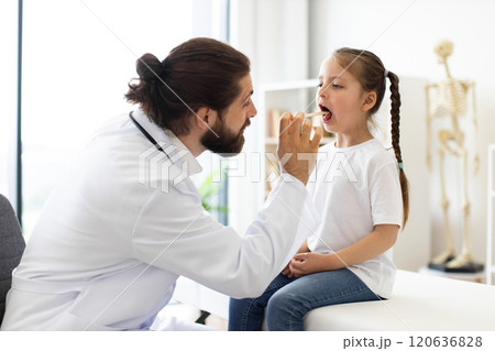 Caucasian doctor examines young girl's throat in medical clinic Caucasian doctor examines young girl's throat in medical clinic 120636828