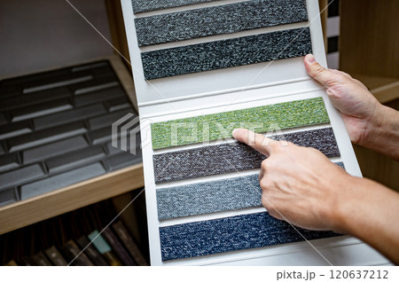 Designer hand pointing at sample fabric pieces on carpet swatch collection 120637212