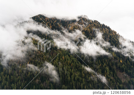 Low clouds in front of an autumn forested peak Low clouds in front of an autumn forested peak 120638056