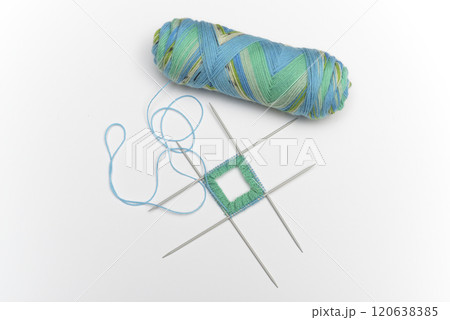 a skein of colorful variegated yarn in shades of blue, green, and yellow, alongside a small knitting project on four double-pointed needles 120638385