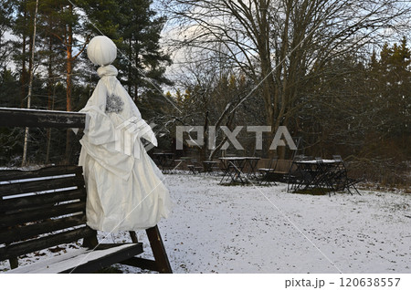 a winter scene in an outdoor setting featuring a rustic bench adorned with a unique handmade figure resembling a snowman or scarecrow 120638557