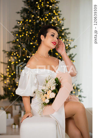 A woman with a bouquet of roses stands near a Christmas tree 120639309