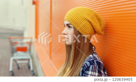 Side portrait of modern young teenage blonde girl in yellow hat on orange background 120639405