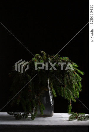 A transparent vase with green fluffy branches of a Christmas tree stands on the table A transparent vase with green fluffy branches of a Christmas tree stands on the table 120639419