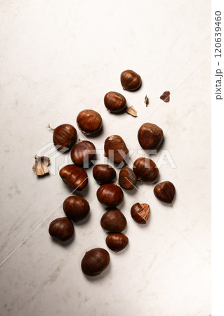 Fresh harvest of edible chestnuts scattered on a white table 120639460