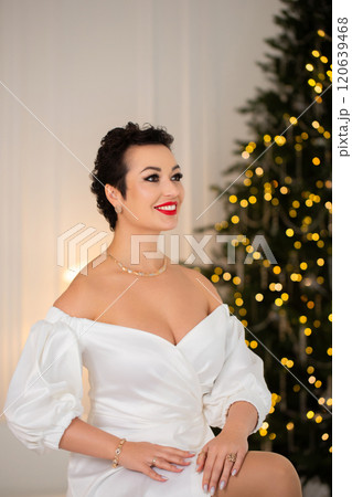 A woman in a white dress sits in front of a Christmas tree A woman in a white dress sits in front of a Christmas tree 120639468