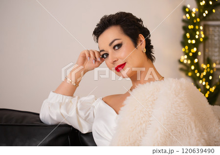 A woman is sitting on a couch with a white fur fur coat over her shoulders. She is wearing a dress and a gold bracelet. A woman is sitting on a couch with a white fur fur coat over her shoulders. She is wearing a dress and a gold bracelet. 120639490