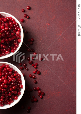 Two bowls of red lingonberries with scattered berries on a burgundy background. Top view 120639630