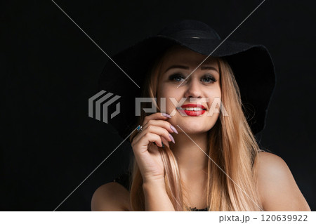 A woman with long blonde hair and a black hat is smiling 120639922