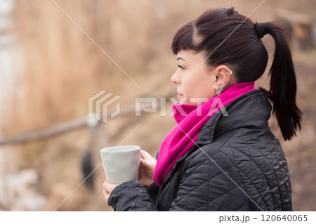 A woman sits on a log , holding a cup of coffee. 120640065