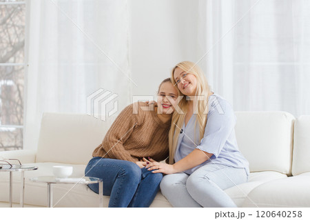 Two women are sitting on a white couch, one of them is wearing a brown sweater Two women are sitting on a white couch, one of them is wearing a brown sweater 120640258