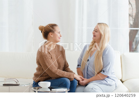 Two women sitting on a couch, one of them holding the other's hand 120640259