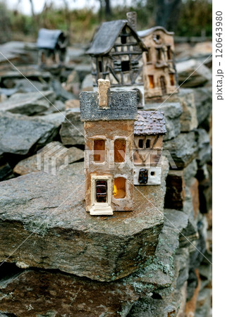 New trends in garden and interior decoration: ceramic houses with glowing windows in modern style. Garden ceramics, miniature. The house placed on old stone wall against rural landscape. Cloudy day. 120643980
