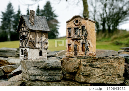 New trends in garden and interior decoration: ceramic houses with glowing windows in modern style. Garden ceramics, miniature. The house placed on old stone wall against rural landscape. Cloudy day. 120643981
