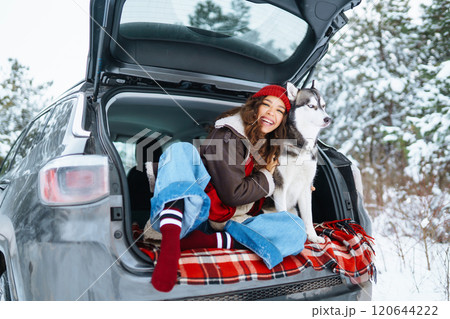 Happy woman with her husky having a picnic in the trunk of a car on a snowy road. Travel concept. Happy woman with her husky having a picnic in the trunk of a car on a snowy road. Travel concept. 120644222
