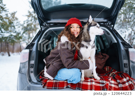 Happy woman with her husky having a picnic in the trunk of a car on a snowy road. Travel concept. Happy woman with her husky having a picnic in the trunk of a car on a snowy road. Travel concept. 120644223