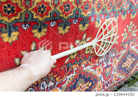 beater knocks dust out of old red asian carpet 120644292