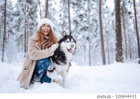 Happy woman walking her dog in the winter and both explore the snow together in playful mood. 120644433