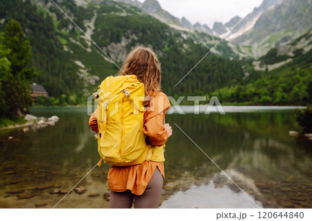 Travel Slovakia, Europe. Tourist with a yellow backpack stands against the backdrop of alpine lake. 120644840
