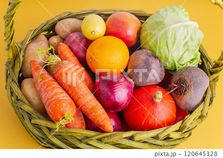 Vegetables and fruits in a wicker basket on a yellow background. 120645328