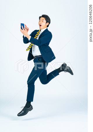 スマホを見ながらジャンプする若い男性ビジネスパーソンの全身写真 120646206