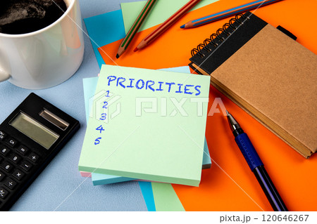 Priorities List. Notepad with text, coffee mug and calculator and stationery on office table Priorities List. Notepad with text, coffee mug and calculator and stationery on office table 120646267