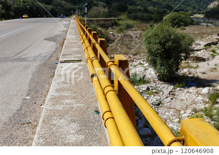 Bright yellow railing along a winding road near a river in a mountainous area 120646908