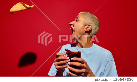 Emotional young woman with short hair, holding glass of mulled wine with crepe pancake flying to her face, set against red background Emotional young woman with short hair, holding glass of mulled wine with crepe pancake flying to her face, set against red background 120647850