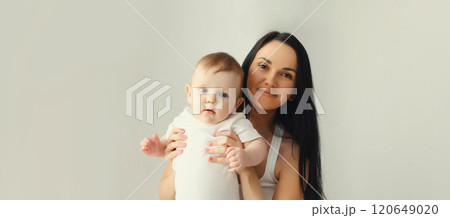 Happy smiling young mother playing with baby in white room at home Happy smiling young mother playing with baby in white room at home 120649020