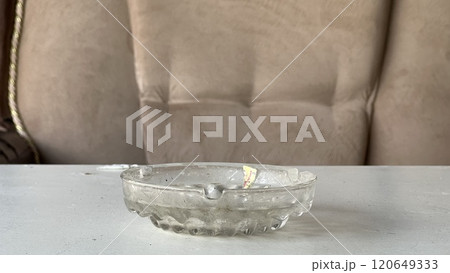 Clear glass ashtray placed on a table beside a soft couch Clear glass ashtray placed on a table beside a soft couch 120649333