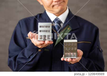 ビルの模型を持って悩む紺色の作業着姿のミドル男性ビジネスマン 120649989