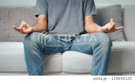 the man is meditating or practicing yoga sitting on a couch with his hands on his knees. the man is meditating or practicing yoga sitting on a couch with his hands on his knees. 120650120