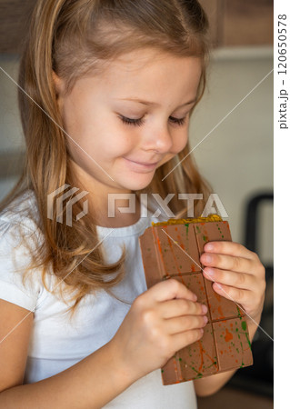 Little girl eating Dubai chocolate with pistachio paste and kataifi dough. Confectionery handmade sweets at home in the kitchen.  120650578