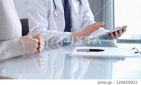 Doctor is consulting patient in modern clinic. Healthcare professional discusses medical information with a woman, using a tablet computer. Medicine concept Doctor is consulting patient in modern clinic. Healthcare professional discusses medical information with a woman, using a tablet computer. Medicine concept 120650922