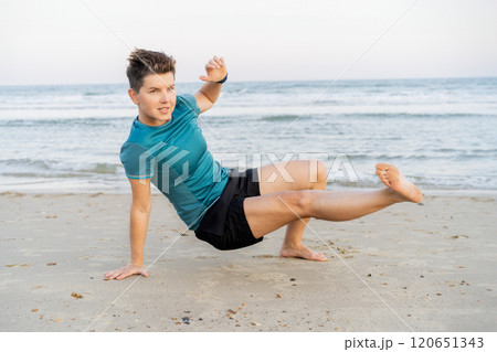 Sporty woman is engaged in animal flow gymnastics outdoors on sea beach. Female trains with Animal Flow workout to elevate her body weight workout. Innovative animal instinct fitness sport movement. 120651343