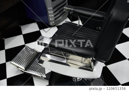 Stylish black barber chair in modern barbershop with checkered floor Stylish black barber chair in modern barbershop with checkered floor 120651356