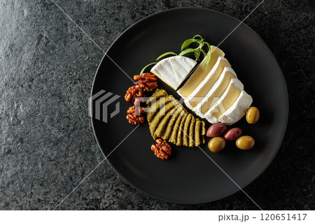 Camembert cream cheese with olives, rosemary, and walnuts on a black plate. Camembert cream cheese with olives, rosemary, and walnuts on a black plate. 120651417