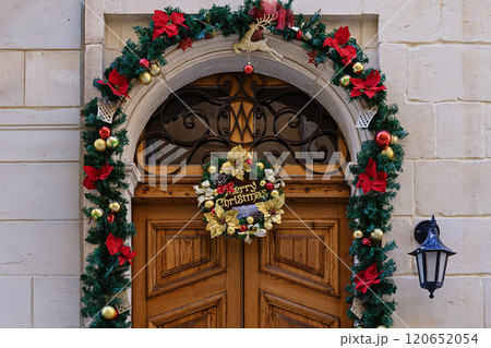 Wooden door decorated with Christmas garlands, wreath, ornaments, and festive lights on a stone building facade Wooden door decorated with Christmas garlands, wreath, ornaments, and festive lights on a stone building facade 120652054