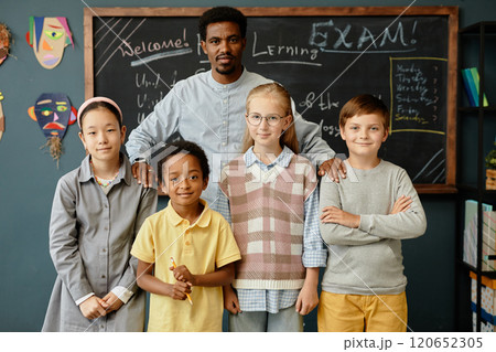Portrait of African American male teacher and four smiling young students standing together at blackboard in classroom 120652305