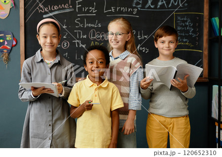 Portrait of four young students from different ethnic backgrounds happily smiling at camera while standing at blackboard in primary school classroom Portrait of four young students from different ethnic backgrounds happily smiling at camera while standing at blackboard in primary school classroom 120652310