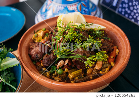 Traditional Moroccan tagine with lamb, vegetables, and nuts served with a fresh side salad. Highlights vibrant Mediterranean flavors and culinary artistry. 120654263