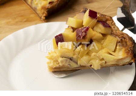 焼きたてのさつま芋とりんごのキッシュをケーキサーバーで皿に乗せる 120654514