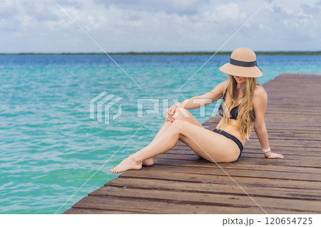Woman in swimsuit sitting on a pier at Lake Bacalar. Quintana Roo, Mexico travel, summer relaxation, and waterfront serenity concept Woman in swimsuit sitting on a pier at Lake Bacalar. Quintana Roo, Mexico travel, summer relaxation, and waterfront serenity concept 120654725